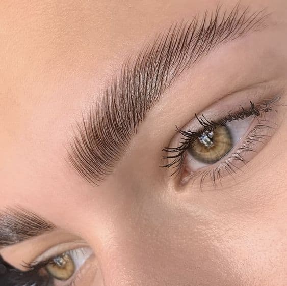 Jeune femme avec une belle manucure, la main sur la joue, une extension de cils ainsi qu'un Brow Lift.