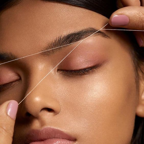 Young well-made-up woman with beautiful eyebrows, two threads visible at eyebrow level, photo taken during eyebrow threading.